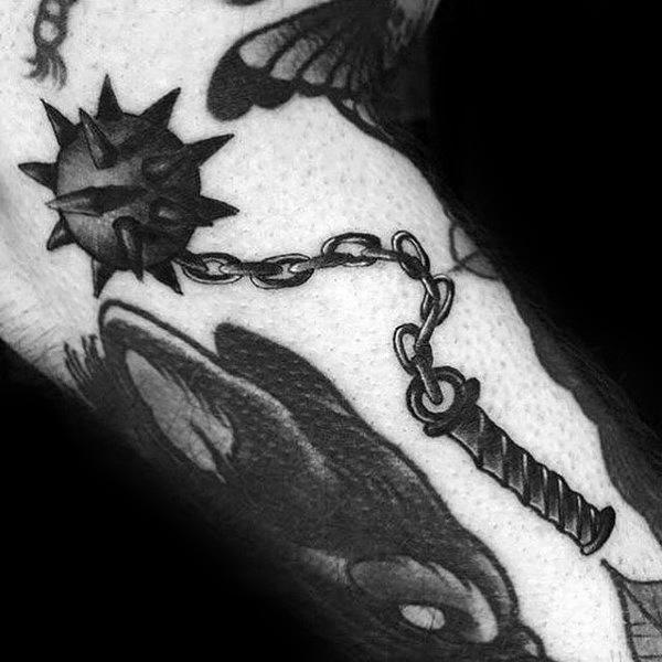 Bold black ink mace tattoo featuring a spiked ball on a swinging chain with a textured handle, symbolizing strength, battle, and resilience.