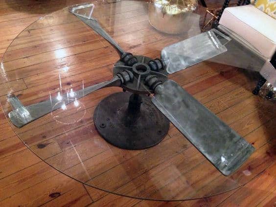 Round glass table with a vintage airplane propeller base on a wooden floor