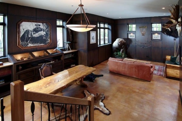 Rustic man cave with a large wooden table, leather couch, bear sculpture, and animal-hide rugs featuring wildlife-themed decor