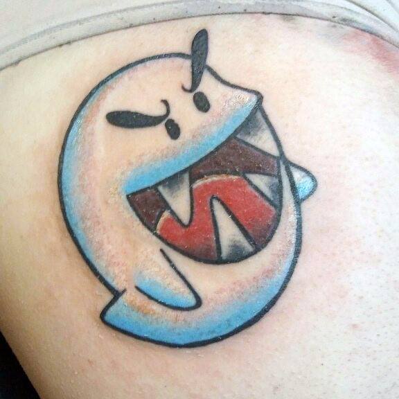 Mario ghost tattoo featuring an angry Boo with a wide-open mouth, sharp teeth, and blue shading, inked on the skin with bold outlines.