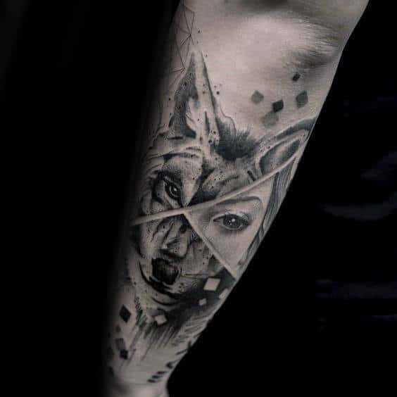 Forearm tattoo featuring a geometric wolf face blended with a human eye, in black and gray ink