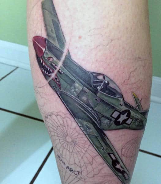 Tattoo of a WWII fighter airplane with shark teeth nose art on a person's leg