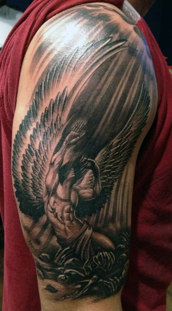 Tattoo of a muscular angel on a shoulder, depicted with wings and dramatic shading