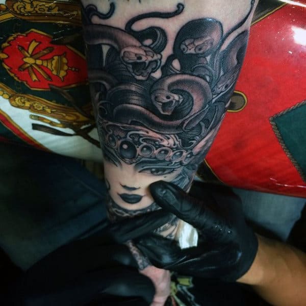 A tattoo artist working on a Medusa-themed forearm tattoo with snake heads