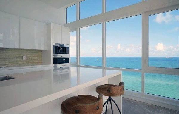 Modern kitchen with ocean view, white cabinets, minimalist design, and barstool seating.