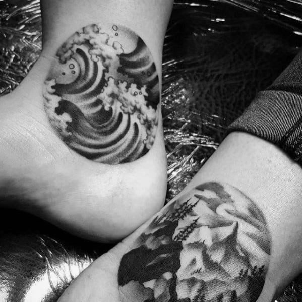 Matching circular tattoos featuring a detailed crashing wave on one ankle and a mountain landscape on the other, symbolizing nature’s balance and contrast.