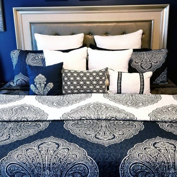 Elegant bed with navy and white patterned bedding and layered decorative pillows.