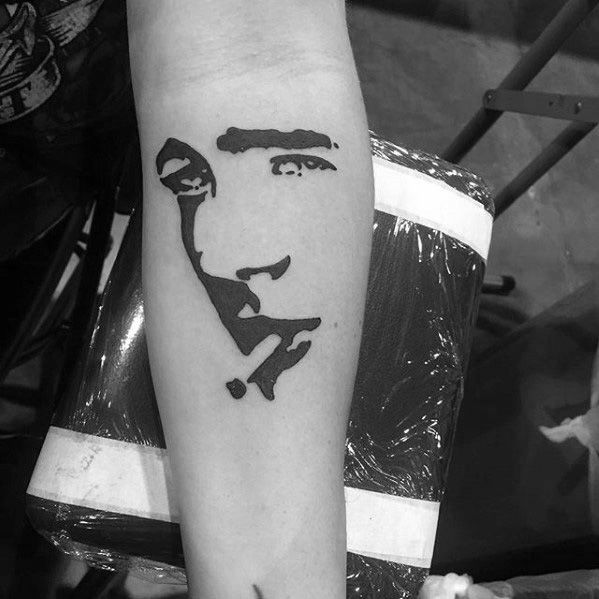 Minimalist black ink tattoo of James Dean’s face created using abstract negative space on the forearm.