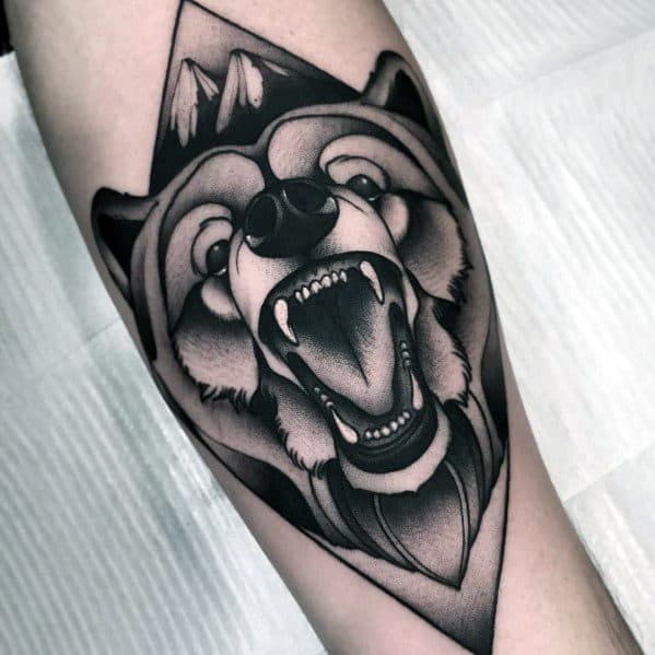 Black and grey neo-traditional bear tattoo featuring a roaring bear framed in a geometric shape with mountain details above its head.