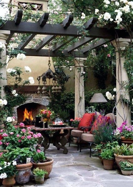 Pergola with stone columns, outdoor fireplace, cozy seating, and colorful potted flowers.