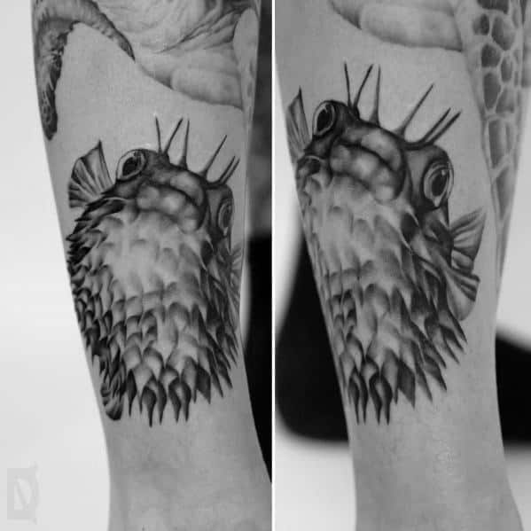 Realistic black and grey pufferfish tattoo with detailed shading and texture, creating a lifelike and dramatic underwater effect.