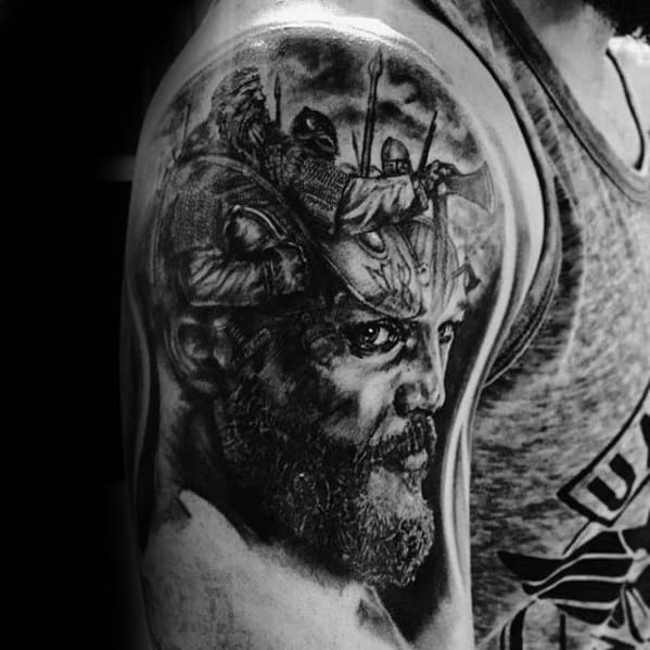 Black and white tattoo of a bearded man on upper arm with warriors on horseback above his head