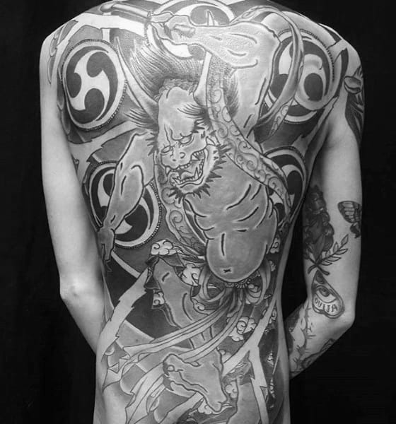 Full back Raijin tattoo in black and grey with bold swirling patterns, dynamic pose, and intense expression of the thunder god.