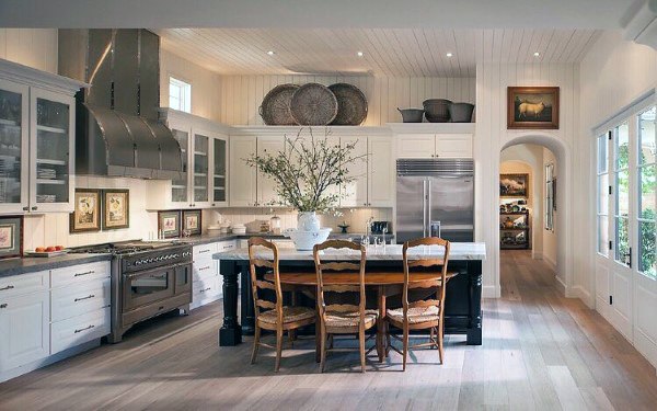 Rustic kitchen with white cabinets, wooden chairs, stainless steel appliances, and a central island.