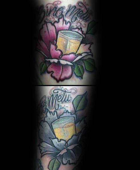 Vibrant shot glass tattoo with a golden drink, nestled inside a blooming flower, featuring bold colors and elegant script for a striking look.