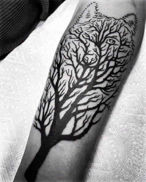Creative Siberian Husky tattoo on a man's forearm, featuring a bold black tree design that forms the shape of a wolf's face within its branches.