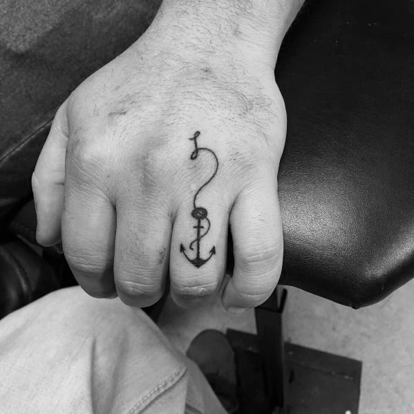 Small anchor tattoo on the finger with a delicate fishing hook design, symbolizing stability, resilience, and a deep connection to the sea.