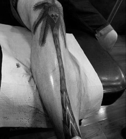 Black ink palm tree tattoo along the leg, with a skull hidden in the leaves, creating a bold and edgy tropical-inspired design.