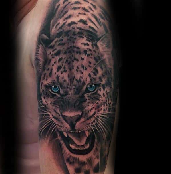 Hyper-realistic snow leopard tattoo on upper arm, showing intense blue eyes and a fierce expression with lifelike fur details.
