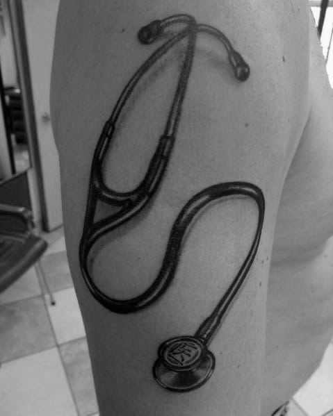 Black and gray stethoscope tattoo on the upper arm, featuring a realistic design that reflects dedication to the medical profession.