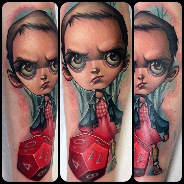 Cartoon-style tattoo of Eleven from Stranger Things with exaggerated eyes, standing beside a red Dungeons & Dragons die.