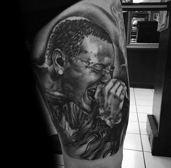 Hyper-realistic black and gray tattoo of Chester Bennington passionately singing, featuring intricate shading and his iconic flame wrist tattoo.