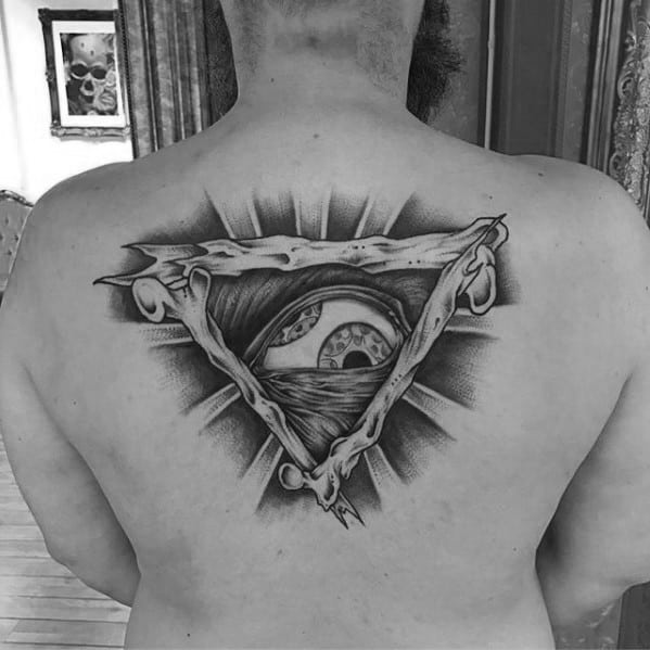 Black and grey back tattoo featuring a detailed eye within a torn triangular frame, radiating light in a surreal, Tool-inspired style.
