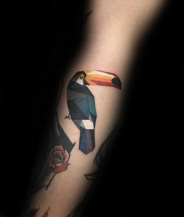 Geometric toucan tattoo with sharp polygonal shapes and bold color blocks on the forearm for a modern, artistic style.
