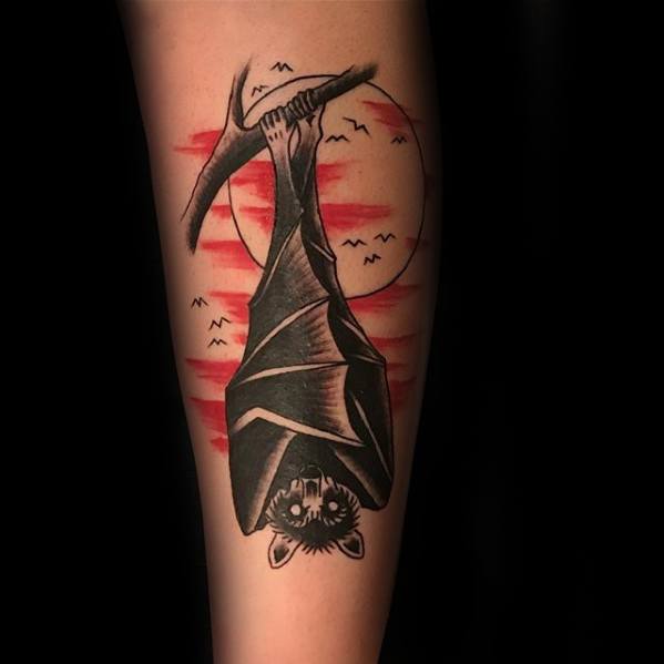 Traditional bat tattoo hanging upside down with red moon and birds in the background, blending bold black and red ink.