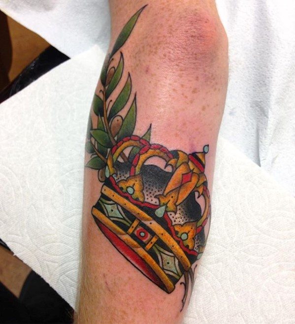Colorful traditional crown tattoo on the forearm with green leaves, red jewels, and bold black shading.