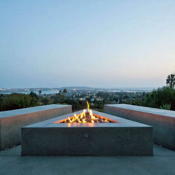 Triangular fire pit on a patio with city lights view in the distance during dusk