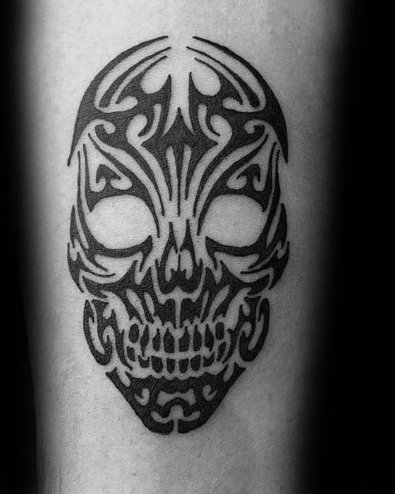 Black tribal skull tattoo with symmetrical patterns and bold lines, combining skull shape and tribal art into a clean, modern design.