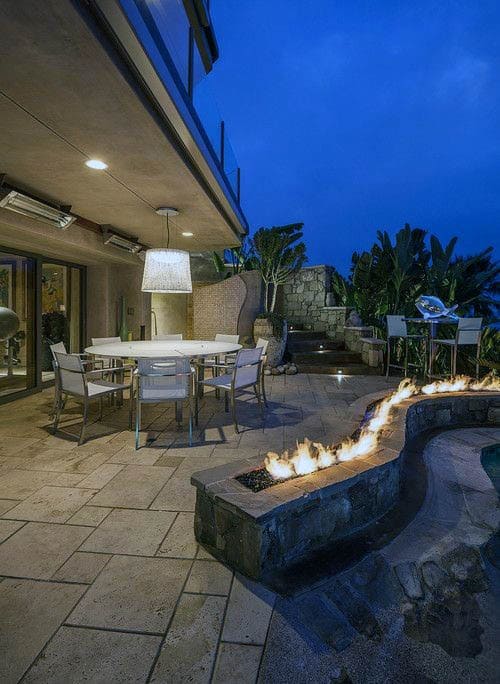 Outdoor patio with a dining table and chairs, fire feature, and tropical plants against a twilight sky