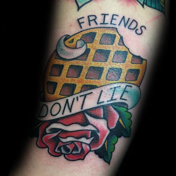Traditional-style waffle tattoo with a banner reading "Friends Don't Lie," a rose, and whipped cream, inspired by vintage and pop culture themes.