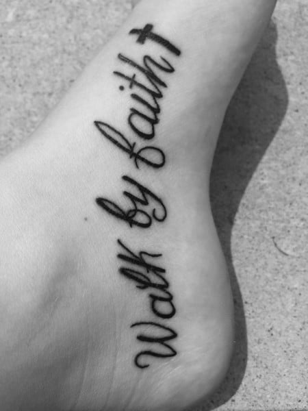Foot tattoo with Walk by Faith in bold cursive script, featuring a small cross at the top, symbolizing trust and spiritual devotion.