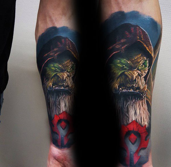 Realistic tattoo of an orc from World of Warcraft with glowing green eyes, a red hood, and the Horde symbol, inked on the forearm.