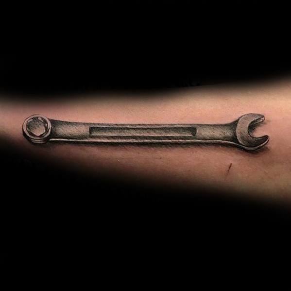 Realistic tattoo of a single metal wrench on the forearm, designed with shading to create a 3D effect.