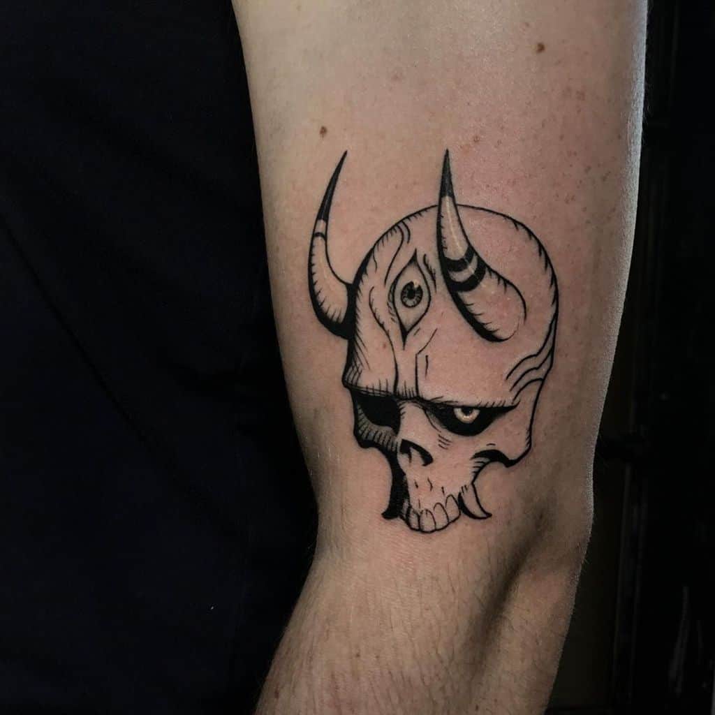 Tattoo of a horned skull with a third eye, inked in bold black lines and shading, placed on the upper arm.