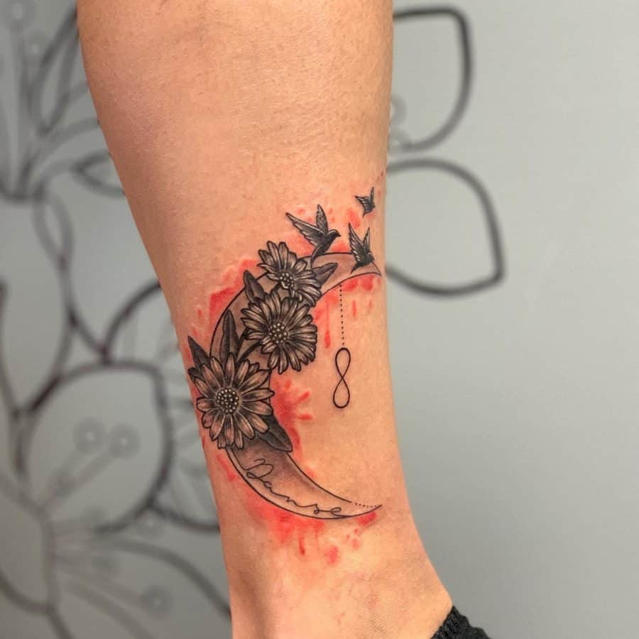 A striking tattoo of a crescent moon adorned with flowers, birds in flight, and an infinity symbol, blending nature and eternity with a touch of red.
