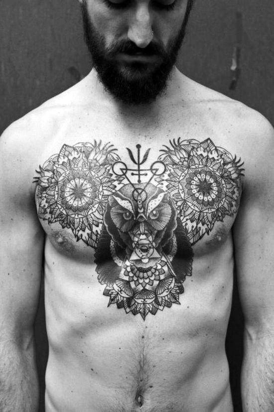 Man with elaborate symmetrical chest tattoos featuring animal and geometric designs