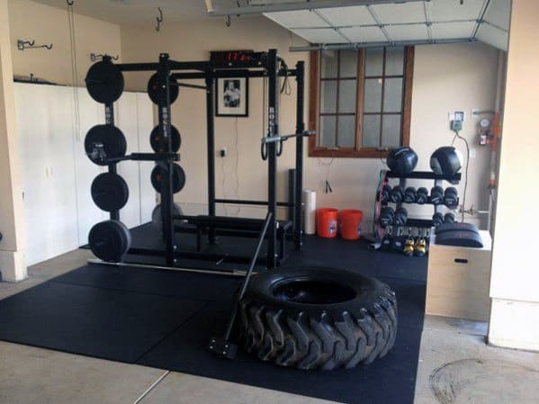 Garage gym with squat rack, weight plates, dumbbells, tire for functional training, and rubber flooring.