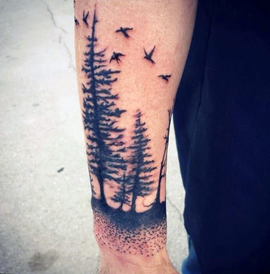Forearm tattoo of pine trees and birds flying in the sky