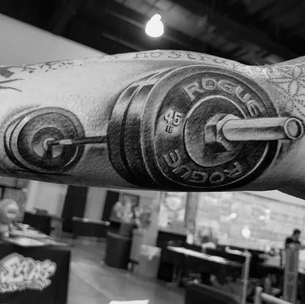 Realistic black and gray barbell tattoo featuring Rogue 45 lb plates, symbolizing strength, dedication to weightlifting, and a passion for fitness.