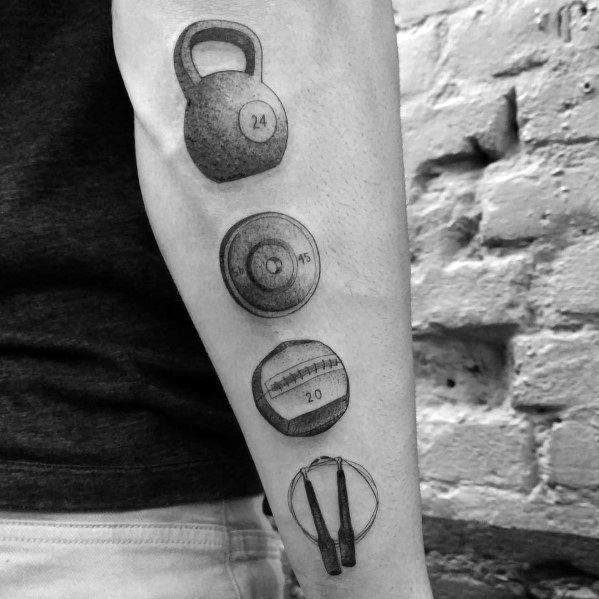CrossFit-inspired forearm tattoo featuring a kettlebell, weight plate, wall ball, and jump rope in detailed black and gray shading.
