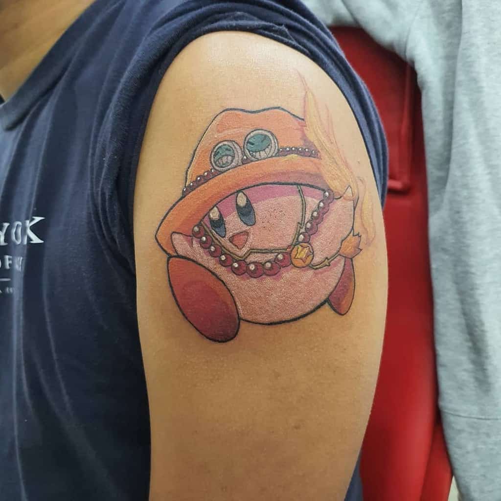 Kirby tattoo wearing Ace’s hat from One Piece, complete with beads and feather, a creative crossover blending both iconic characters