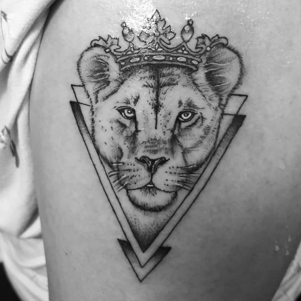 Black and grey lioness tattoo on the thigh, featuring a crowned lioness within a geometric triangle for a regal and powerful design.