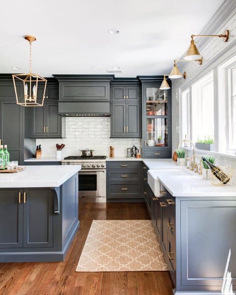 A modern kitchen with elegant crown molding, navy blue cabinetry, marble countertops, and stylish lighting fixtures