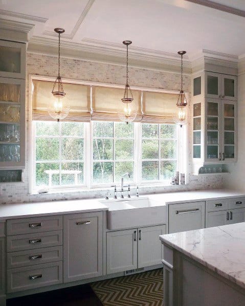 A bright kitchen with elegant crown molding, modern pendant lighting, white cabinetry, and a scenic window view
