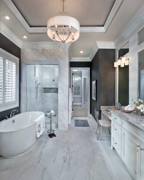 A luxurious master bathroom featuring a trey ceiling with crown molding, a freestanding bathtub, marble flooring, and modern lighting fixtures