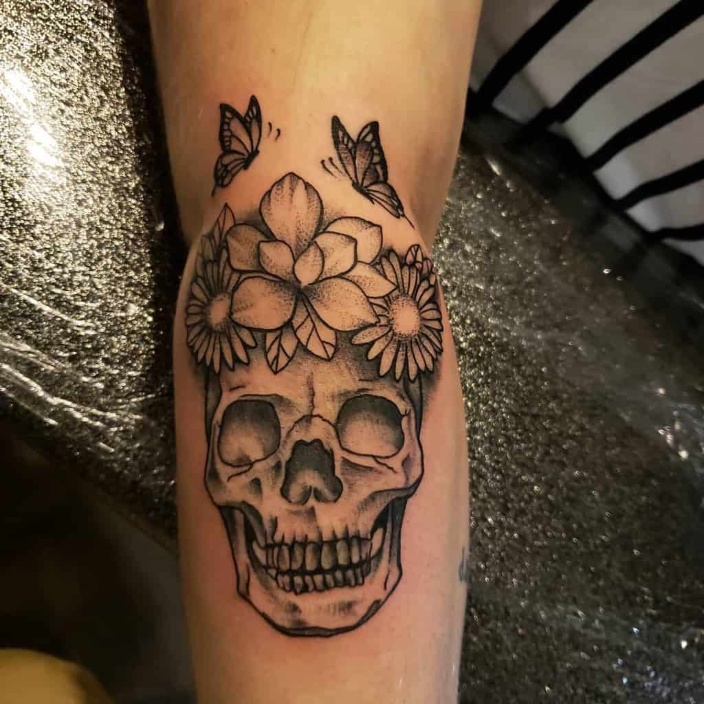 Forearm tattoo black and grey shading skull with crown of daisies and butterflies